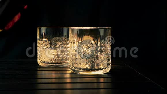 酒吧老板把威士忌倒在两个杯子里木桌上放冰块背景黑色重点放在冰块上威士忌视频的预览图