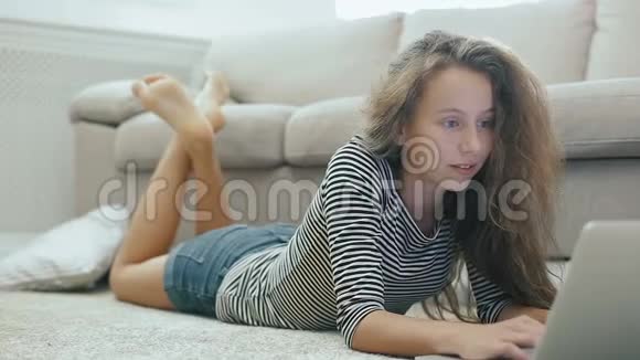 地毯上可爱的少女用笔记本电脑工作stadicam拍摄的快乐少女靠近一个有笔记本电脑的沙发少女使用视频的预览图