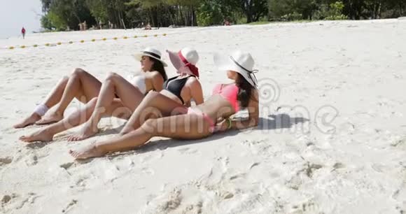 三个女孩躺在比基尼和草帽海滩上享受阳光聊天快乐的女性游客在暑假视频的预览图