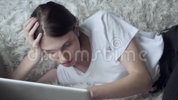 微笑的女人在家里躺在沙发上用笔记本电脑视频的预览图