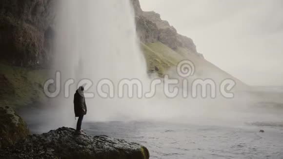 带着动作镜头的年轻人站在冰岛的Gljufrabui瀑布附近拍摄水流的视频视频的预览图