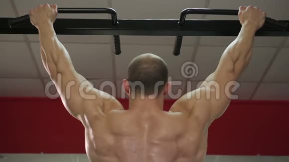 强壮的男性运动员的后视图肌肉发达的手臂和肩膀挂在酒吧上视频的预览图