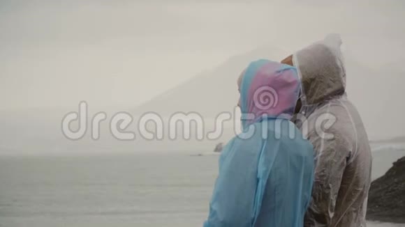 年轻夫妇穿着雨衣站在冰岛的冰湖里用手指向对方展示一些东西视频的预览图
