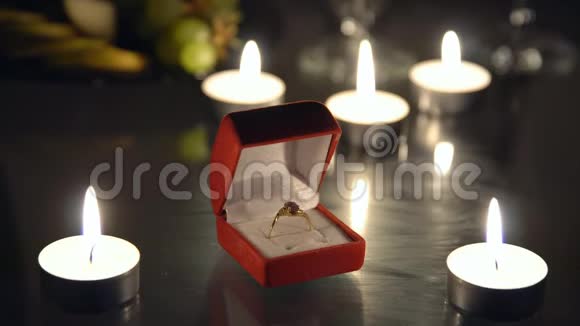 在点燃蜡烛的背景下在红色盒子里特写一枚戒指视频的预览图