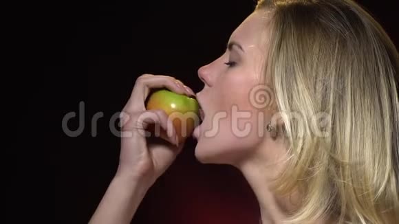 一个漂亮的金发女郎咬了一口绿色的苹果转向相机视频的预览图