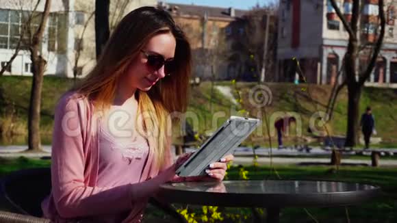 年轻女性在公园里享受社交网络用平板电脑聊天视频的预览图