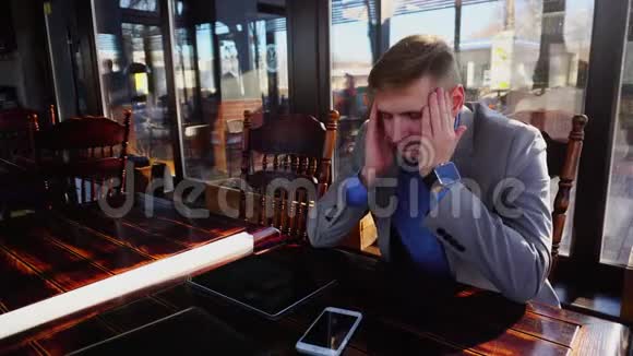 年轻疲惫的经理在咖啡馆休息桌上放着卷纸平板电脑和智能手机视频的预览图