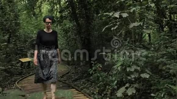 4K美丽的女孩穿着黑色手工裙的方形纹理在绿色森林深处的一条木道上污秽不堪视频的预览图