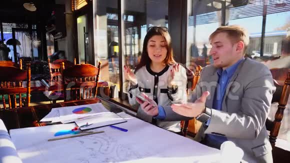 男性建筑师建议女性平面设计师使用项目和智能手机在咖啡馆视频的预览图