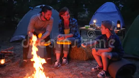 带着帐篷旅行在森林里野餐家人围着火晚上准备黄色玉米妈妈儿子和爸爸在晚上视频的预览图