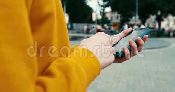近距离观看不知名男手穿黄色毛衣在手机户外发短信和浏览4K录像视频的预览图