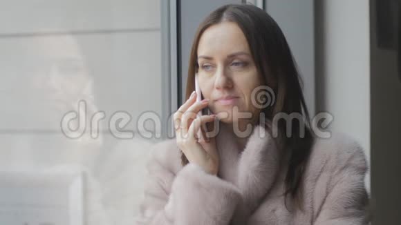 穿着鲜艳外套的女孩在窗口用手机说话视频的预览图