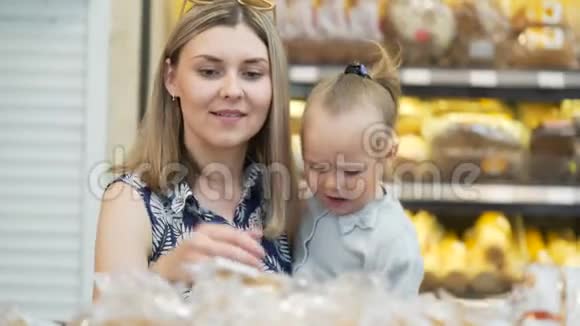 年轻妈妈抱着小女儿拿起羊角面包用钳子近距离夹住视频的预览图