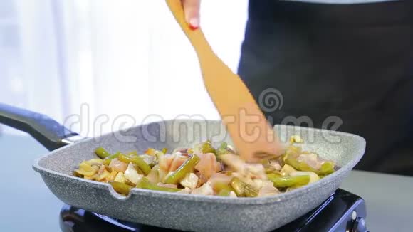 一个女人在煎锅里把木铲和鸡片和豆子和蘑菇混合在一起视频的预览图