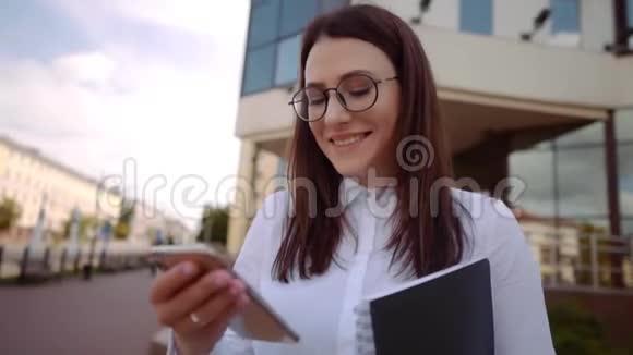 在城市街道上微笑的商务女性穿着白色衬衫使用智能手机慢镜头视频的预览图