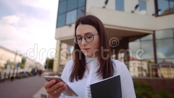 商业女性穿着白色衬衫在城市街道上使用智能手机的正面视图慢镜头视频的预览图
