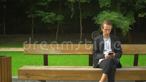 年轻人用智能手机在公园里休息视频的预览图