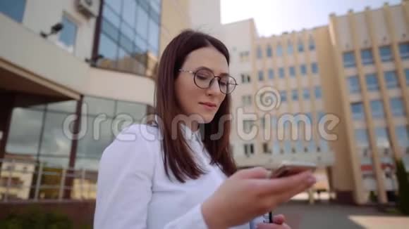 商业女性穿着白色衬衫在城市街道上使用智能手机的正面视图慢镜头视频的预览图