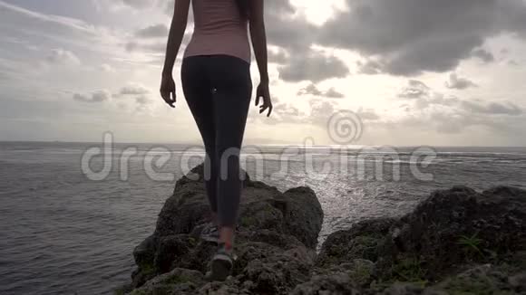 年轻女子张开双臂站在岩石上望着大海视频的预览图