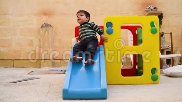 可爱的两岁男孩脏兮兮的从嘴边的饼干滑下塑料滑梯玩房子视频的预览图