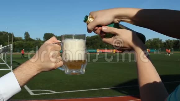 一个男人在一个足球场的背景下把啤酒倒在杯子里在那里他们踢足球特写镜头视频的预览图