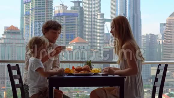 一家人在阳台上吃早餐俯瞰市中心的摩天大楼视频的预览图