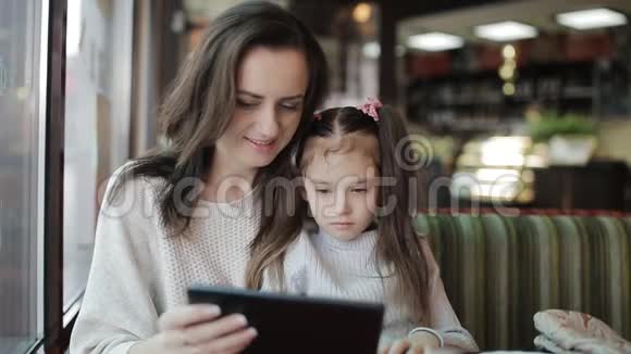 一个小女孩在咖啡馆的平板电脑上使用WiFi妈妈和女儿手里拿着一个小玩意视频的预览图