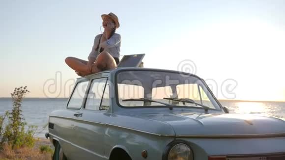 女孩坐在复古的车顶背光在手机上说话手持太阳能阵列年轻女子使用太阳能视频的预览图