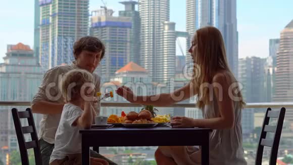 一家人在阳台上吃早餐俯瞰市中心的摩天大楼视频的预览图