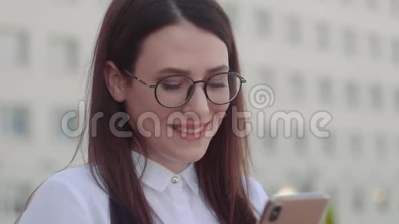 在城市街道上微笑的商务女性穿着白色衬衫使用智能手机慢动作镜头视频的预览图