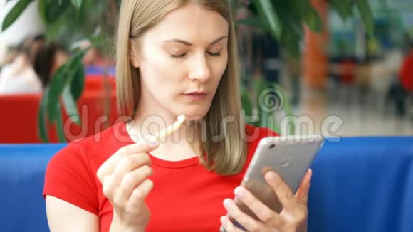穿着红色t恤的女人坐在咖啡馆里用智能手机和朋友聊天吃炸薯条视频的预览图