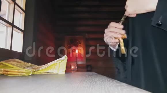 正教的牧师在暮色中穿着神圣的衣服站在木教堂祭坛的窗户前视频的预览图