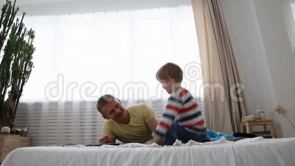快乐的现代家庭爸爸和一个小儿子在卧室的床上玩得很开心视频的预览图