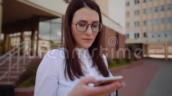 商业女性穿着白色衬衫在城市街道上使用智能手机的正面视图慢动作镜头视频的预览图