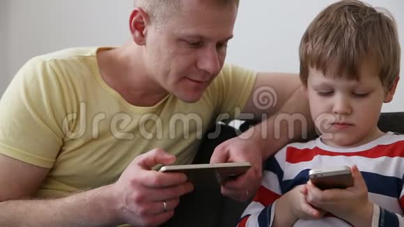 现代家庭生活中的装置爸爸和一个小儿子在智能手机上玩游戏坐在家里的沙发上视频的预览图