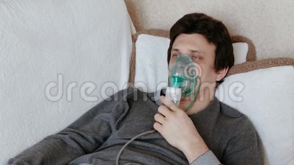 使用雾化器和吸入器进行治疗躺在沙发上的年轻人通过吸入器面罩吸入正面观点视频的预览图