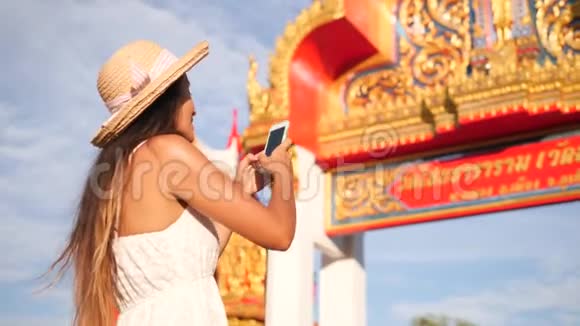 泰国佛寺入口门的年轻混血少女用手机拍照普吉岛视频的预览图