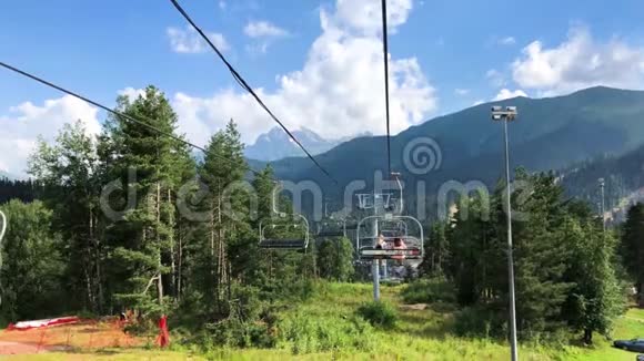 明亮的夏季色彩斑斓的山景蓝色的多云天空和滑雪电梯与两个女人从电梯上看视频的预览图