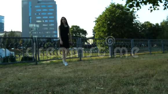 美丽的瘦小的黑发女郎在傍晚的绿草地上慢慢地走着视频的预览图