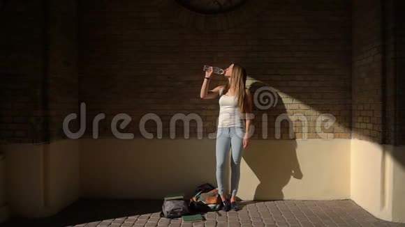 全长视野少女穿着休闲服饮水从瓶身背景的砖墙视频的预览图