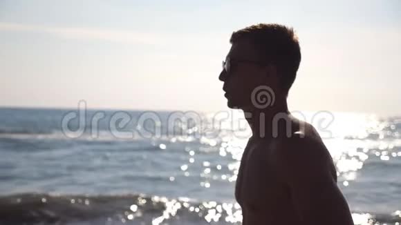 戴墨镜的运动员在海边慢跑的情况阳光明媚的一天年轻的运动员在海滩上奔跑视频的预览图