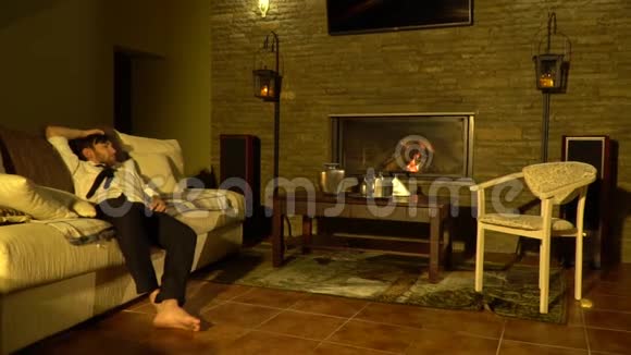 一个光着脚的困人在有壁炉的房间里的沙发上醒来视频的预览图