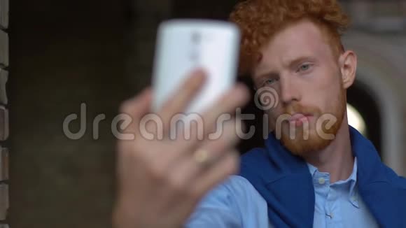 迷人的自信姜头男人留着胡子正在通过手机户外自言自语视频的预览图