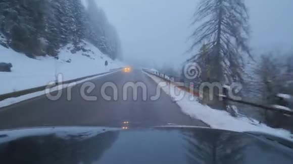 黑暗的现代汽车在农村地区的道路上行驶在白雪覆盖的树木和山丘上视频的预览图
