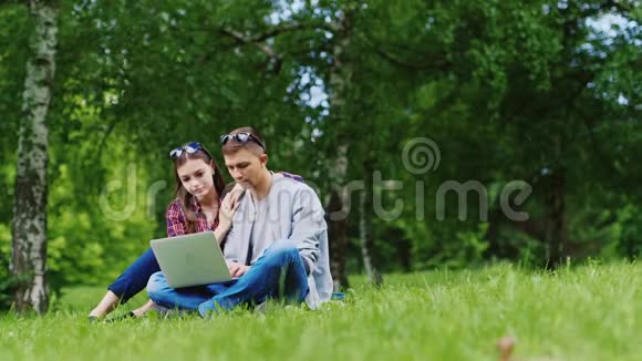 男女朋友坐在公园的草地上享受一台笔记本电脑视频的预览图