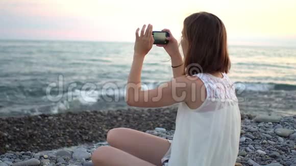 年轻女子用智能手机在海滩上拍船照视频的预览图