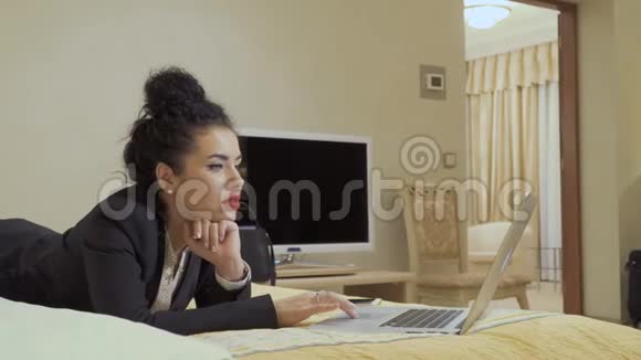 时尚女商人在酒店房间的床上使用笔记本电脑视频的预览图