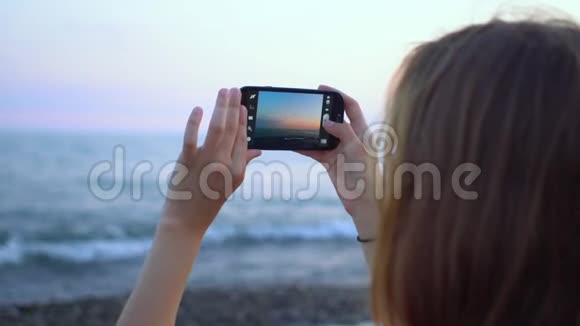 年轻的时髦女人在海边的智能手机上拍照视频的预览图