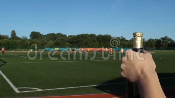 一个男人在足球场的背景上打开一瓶啤酒在那里他们踢足球特写镜头视频的预览图