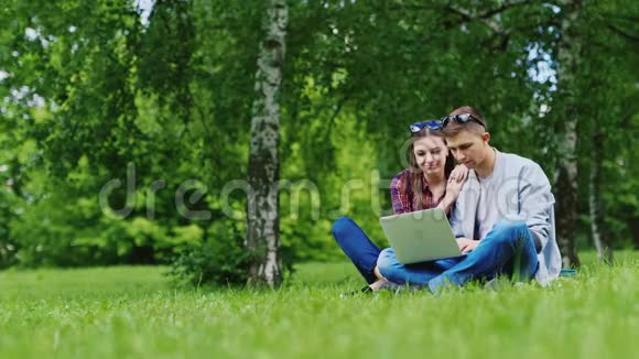 男女朋友坐在公园的草地上享受一台笔记本电脑视频的预览图
